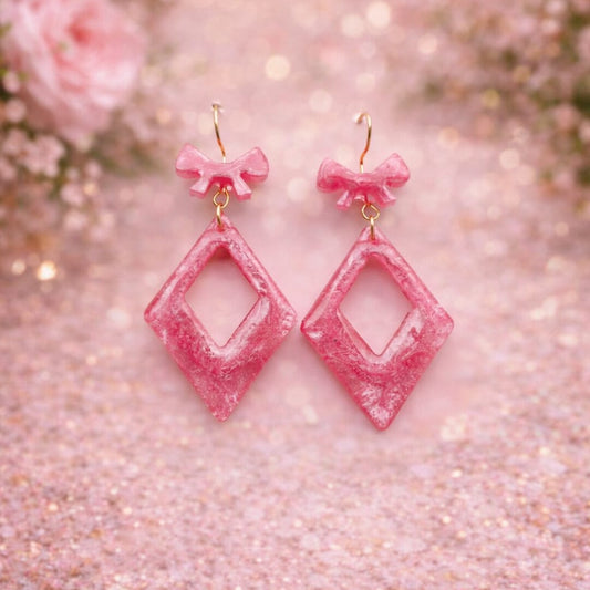 Pink glittery earrings with bow accents on a sparkling pink background